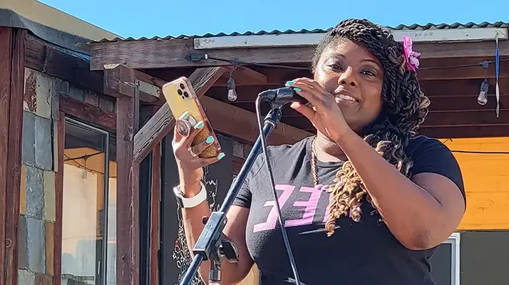 woman on stage speaking into a microphone and holding cell phone
